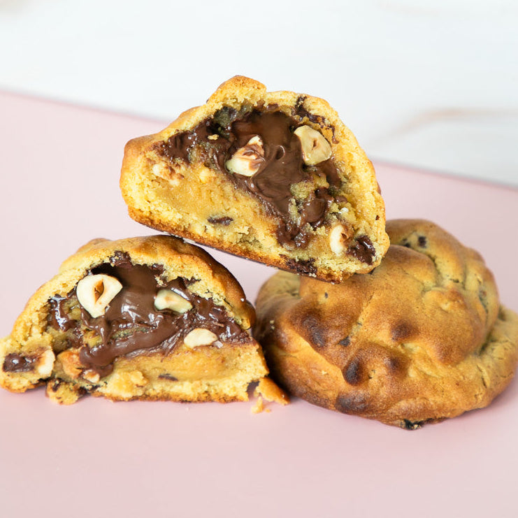 Three chocolate chip cookies with one cut open to reveal a chocolate filling on a pink plate.