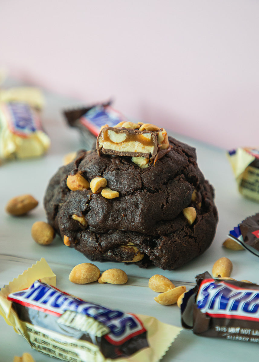 Snickers Chocolate cookie with peanut butter cup on top, surrounded by Snickers candy bars.