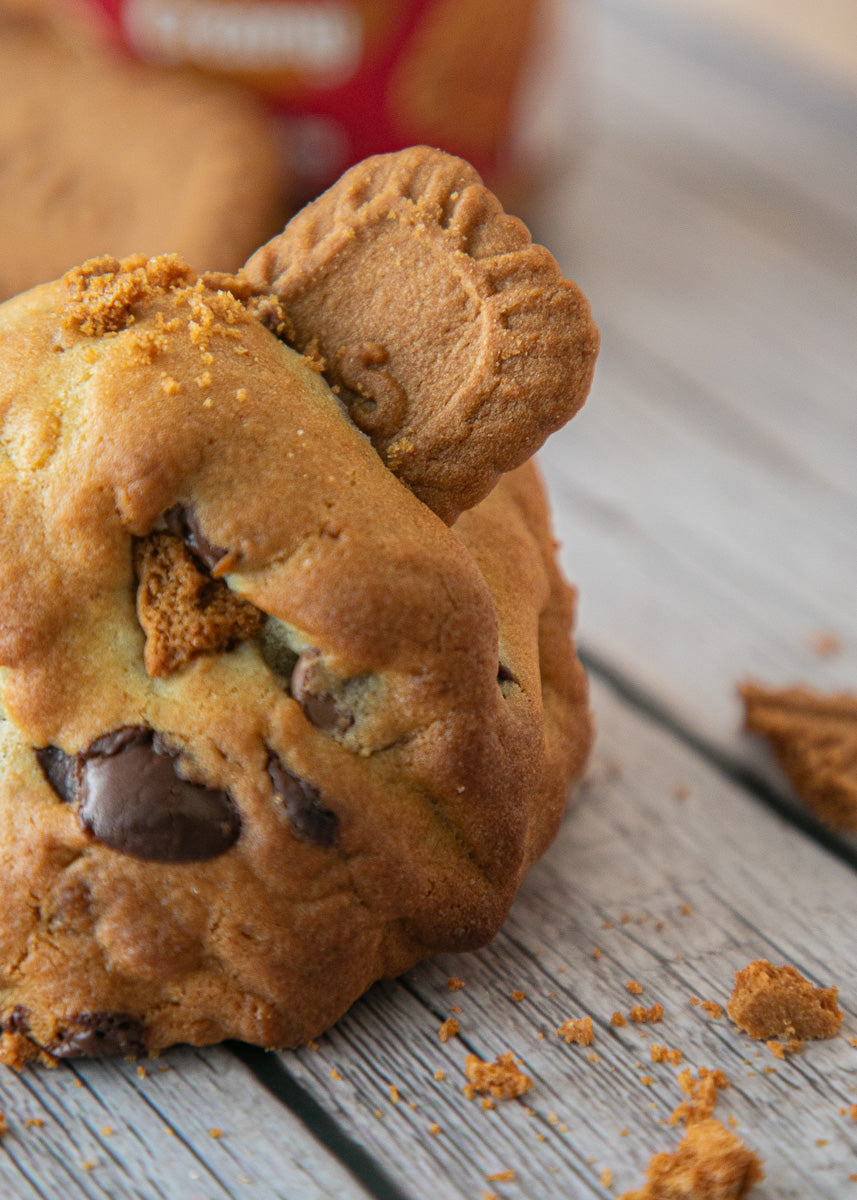 Cookie with chocolate chips and a half lotus cookie on top, placed on a wooden surface.