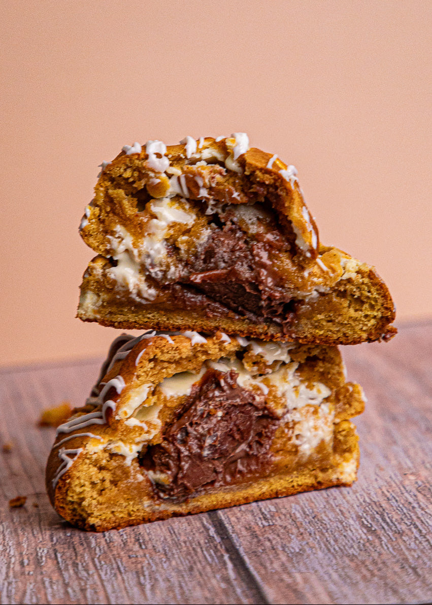 Two-layered Golden Pumpkin cookie on a wooden surface, spiced pumpkin cookie with white chocolate chips and salted caramel filling, cozy fall dessert.